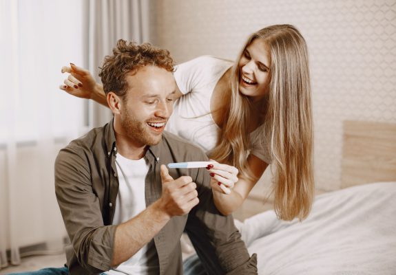Pareja sonriente mirando un test de embarazo positivo en el dormitorio