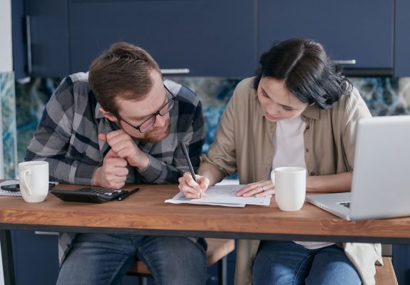 Pareja haciendo cuentas en la mesa de la cocina con una calculadora y un portátil