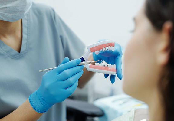 Dentista explicando con un modelo dental el tratamiento de implantes a una paciente