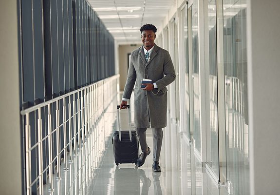 Hombre con traje, maleta y pasaporte caminando por la terminal de un aeropuerto